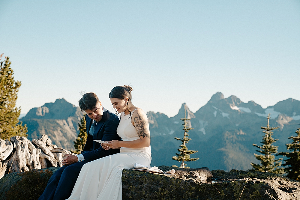 Bride and groom sitting next to each other on a rock while reading letters.