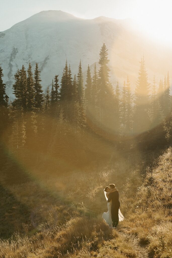 Golden hour sunset elopement photo of a bride and groom on a trail with Mount Rainier in the background.