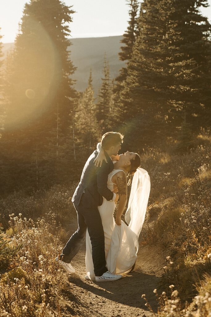 Groom holding bride while she laughs on a hiking trail in Mount Rainier at sunset.