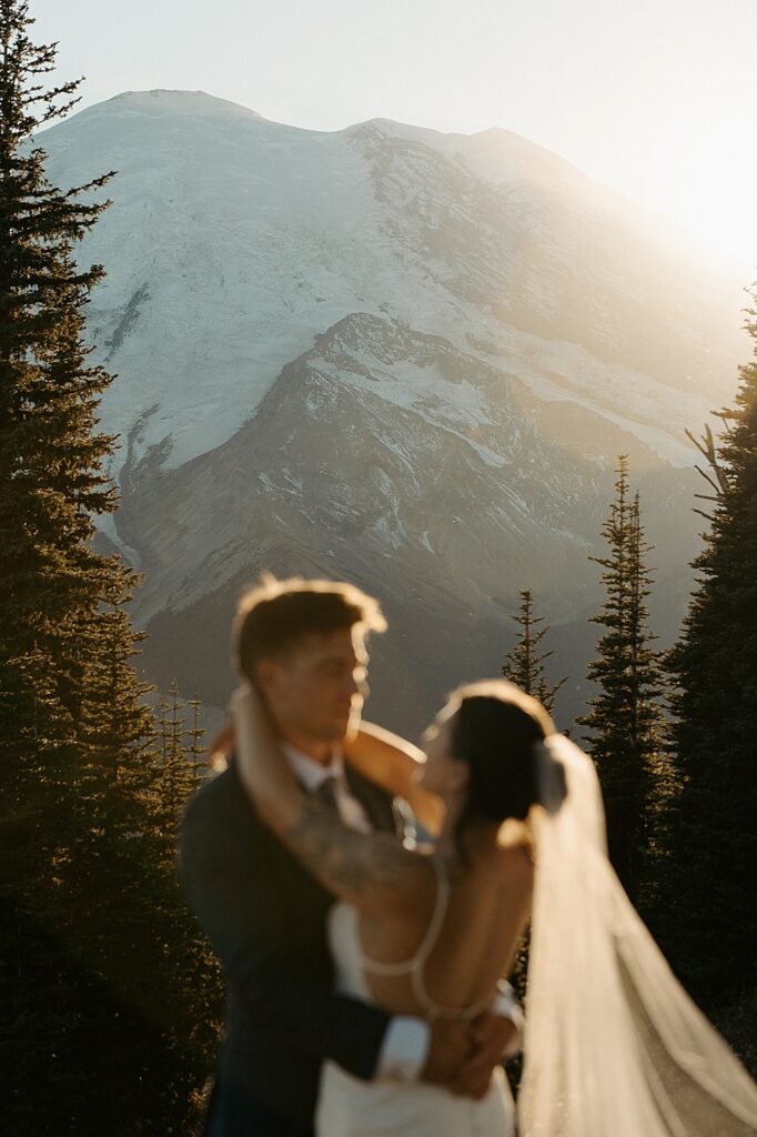 Blurry image of bride and groom holding each other with Mount Rainier in the background at sunset.