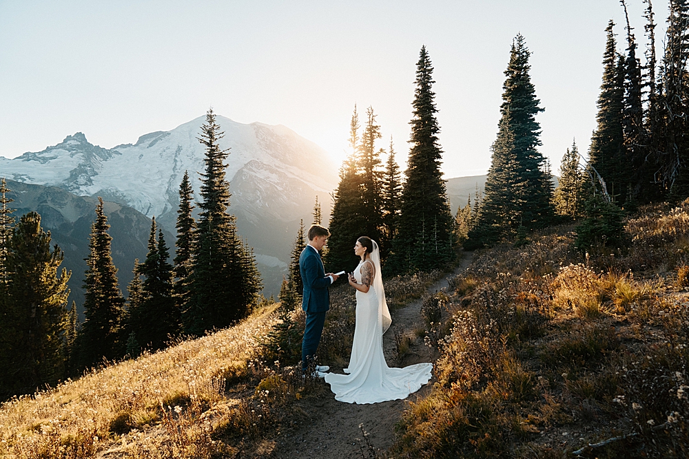 Bride and groom saying vows along a trail at Mount Rainier with the sunset and mountain in the background.