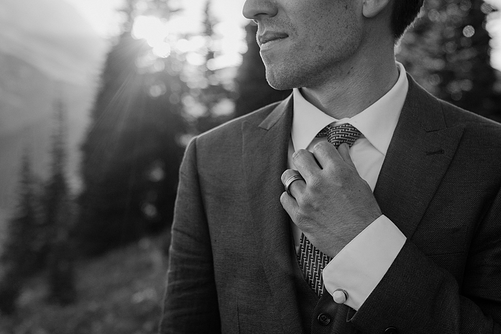 Black & white of groom adjusting his tie.