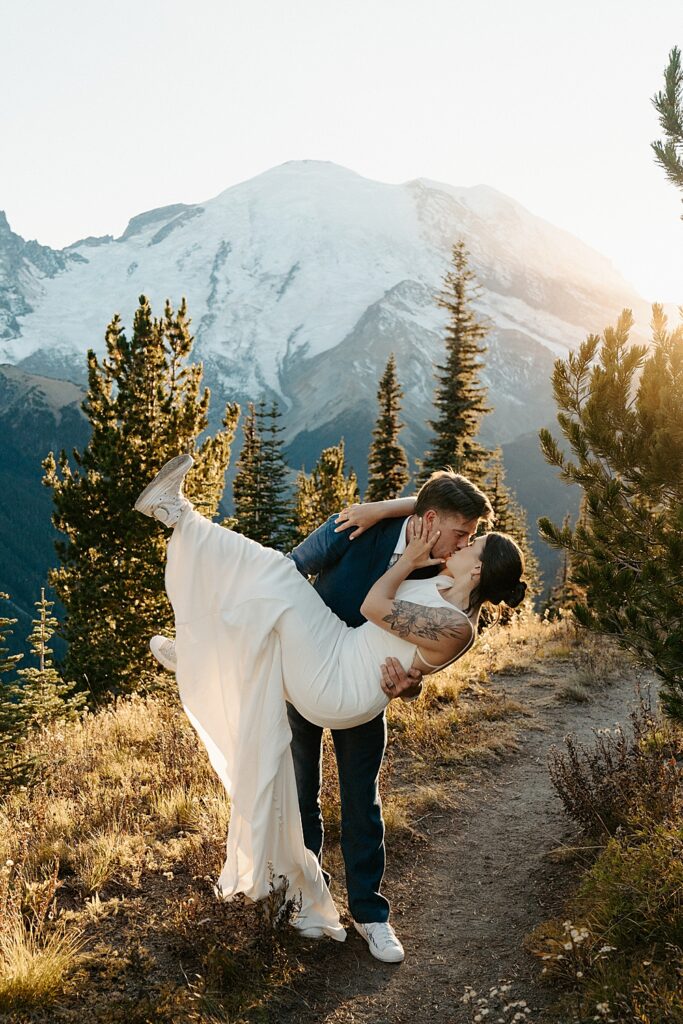 Groom holding his bride, dipping her, and kissing at sunset with Mount Rainier in the background.