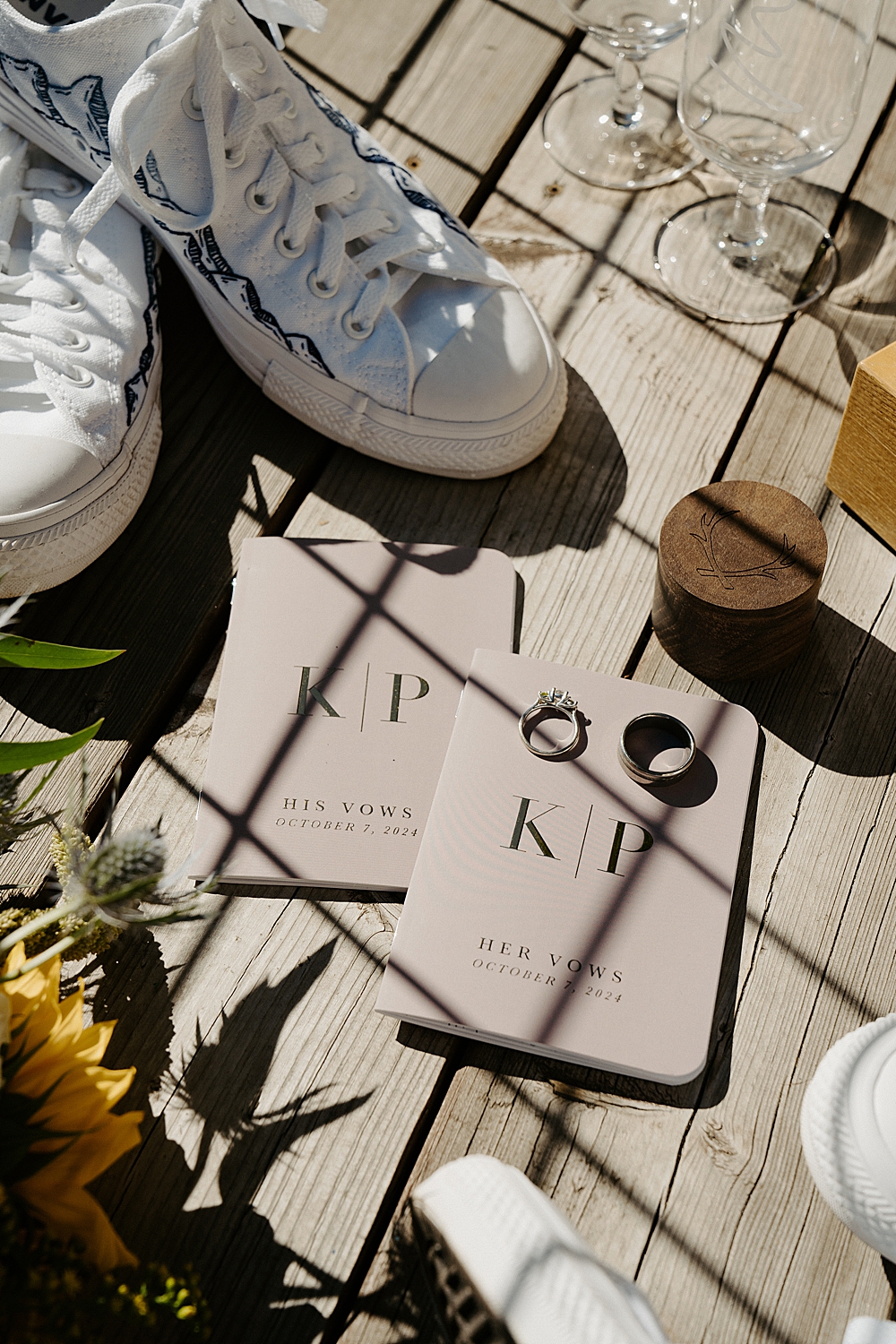 Wedding details with custom vow books, wedding rings, a wooden ring box, and some embroidered Converse.