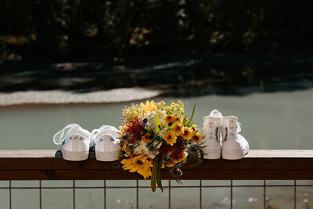 Two pairs of hand-embroidered white converse sitting on a railing with a floral bouquet in the middle.
