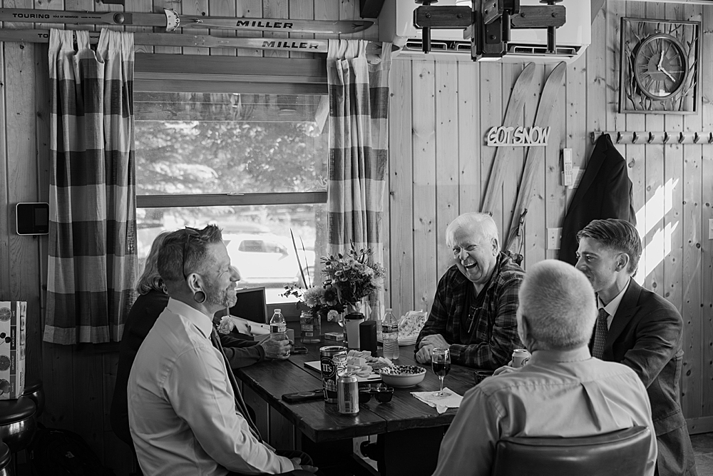 Black & white of groom and family members sitting at table inside a Packwood cabin.