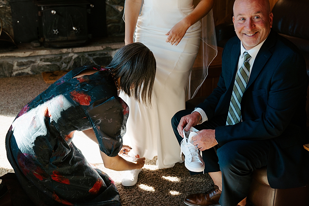 Mother and father of the bride helping her into her white wedding Converse.