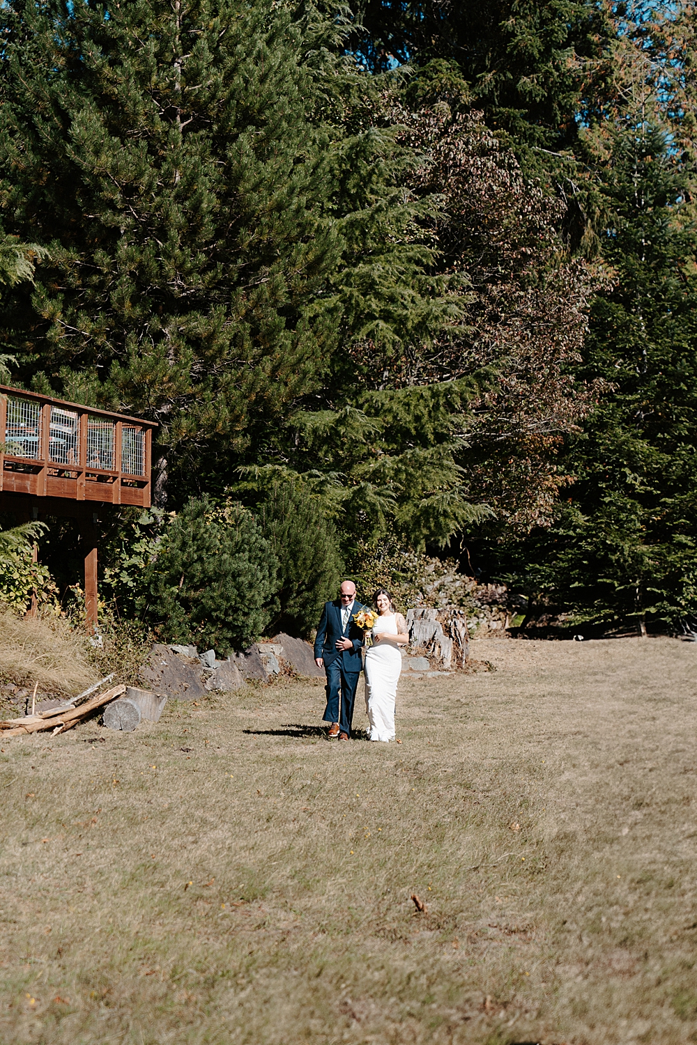 Bride and father of the bride walking on a grassy front lawn to the ceremony location.