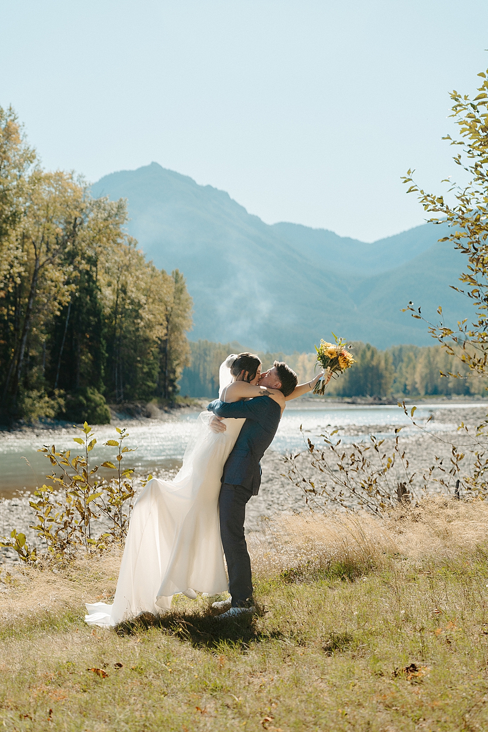Groom in a navy blue suit picking up his bride and sharing a first kiss together.