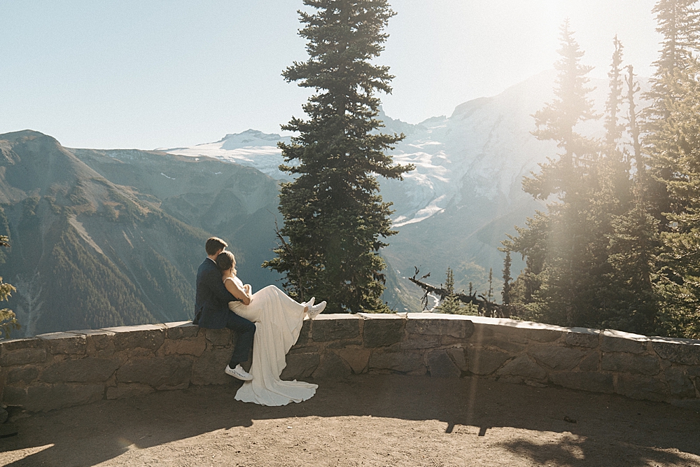 Bride and groom sitting on a short rock wall looking out at Mount Rainier in the later afternoon sun.