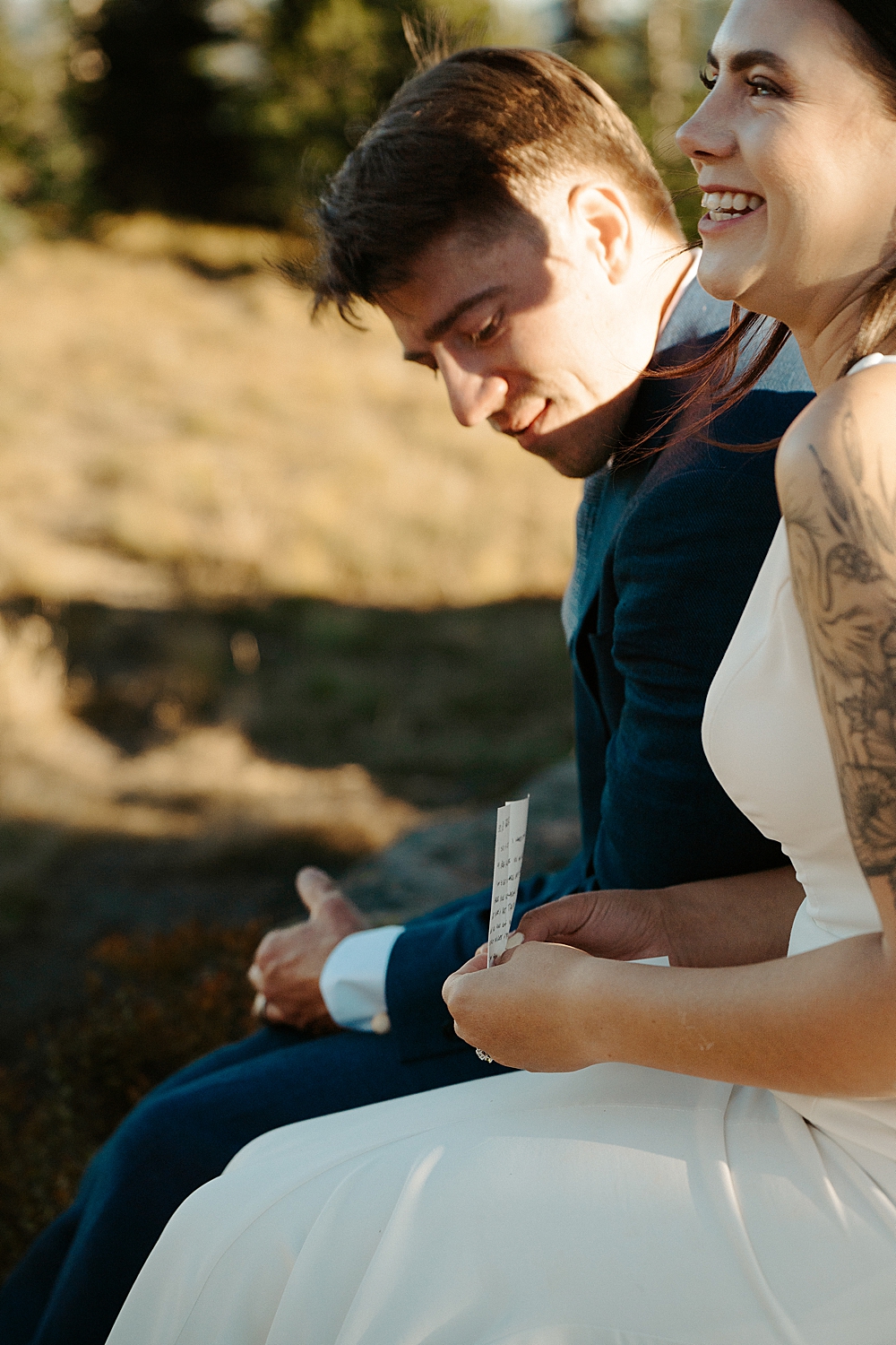 Up close of bride sitting and smiling while holding a letter and her groom sitting behind her.