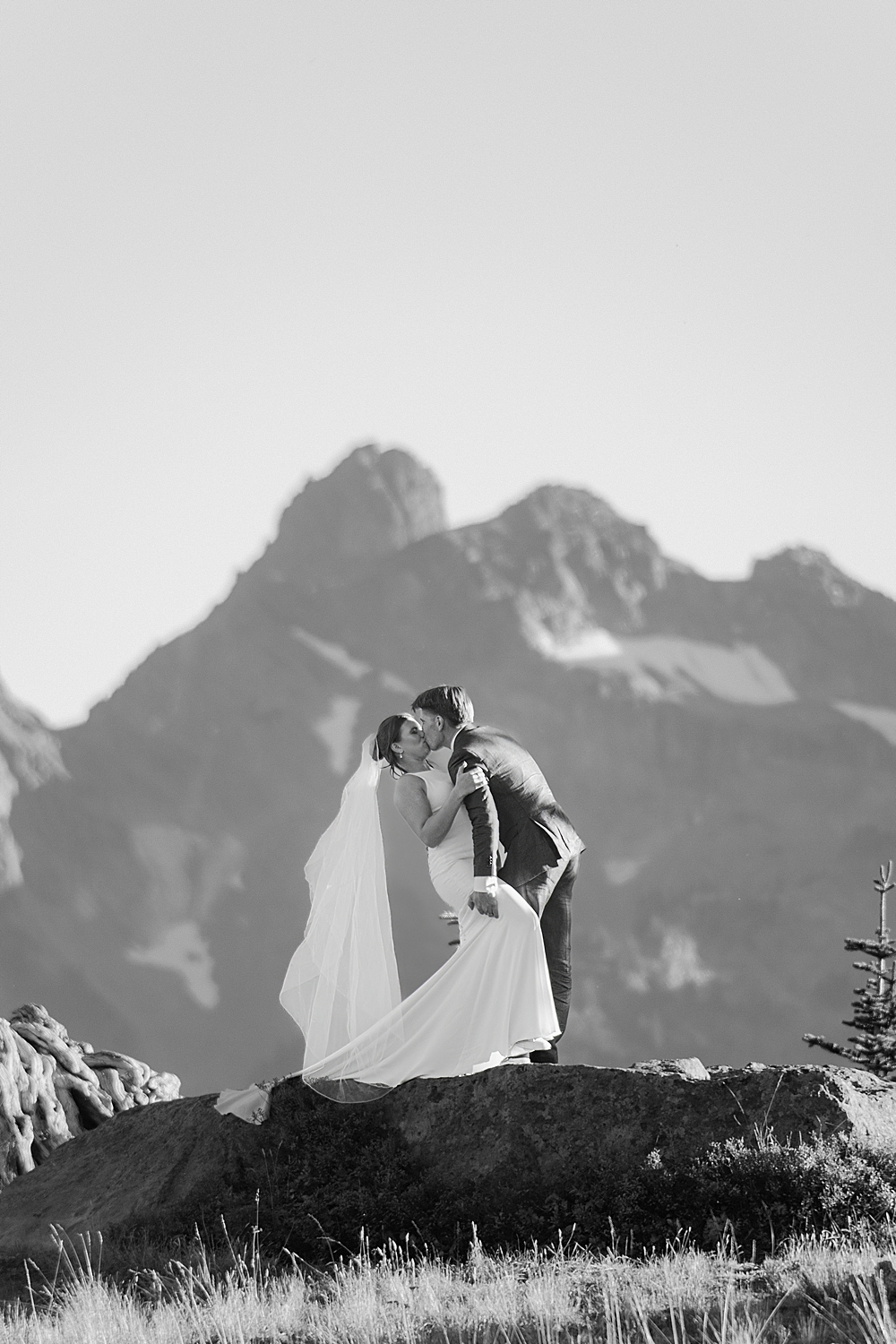Black & white of a bride and groom kiss dipping on a rock in Mount Rainier National Park.