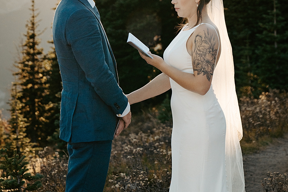 Bride saying vows to her groom while holding his hand and a vow book.