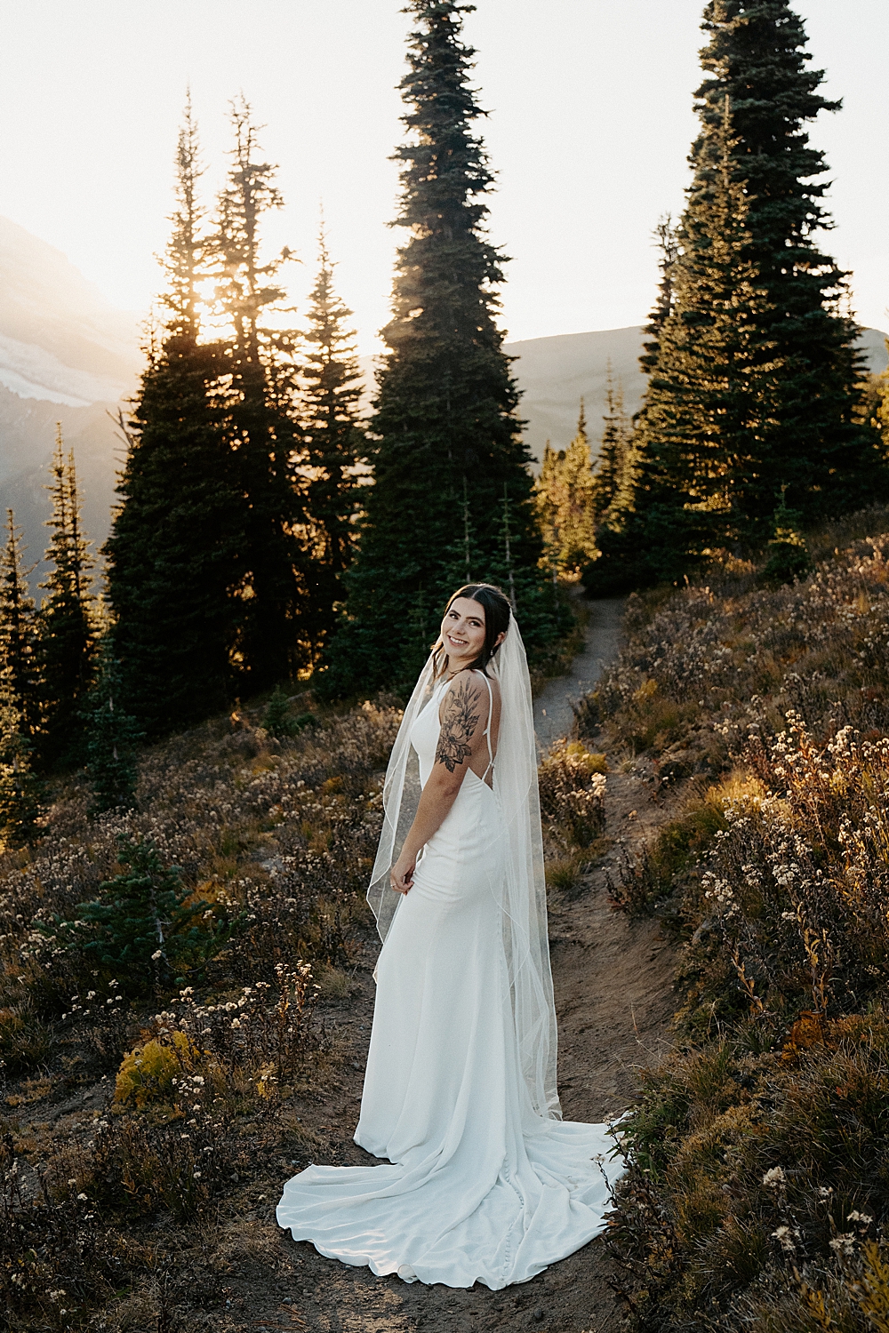 Elopement portrait of a bride in a white satin dress with a long veil at Mount Rainier during sunset.