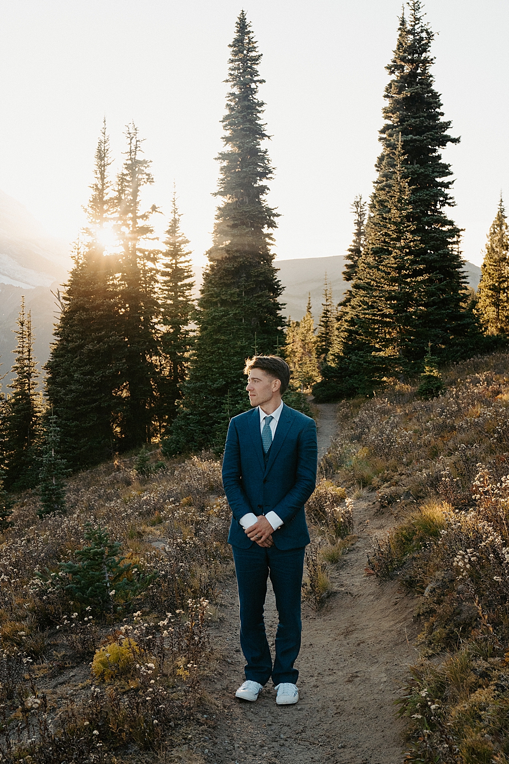 Mount Rainier elopement portrait of a groom in a navy blue wedding suit on a trail at sunset.