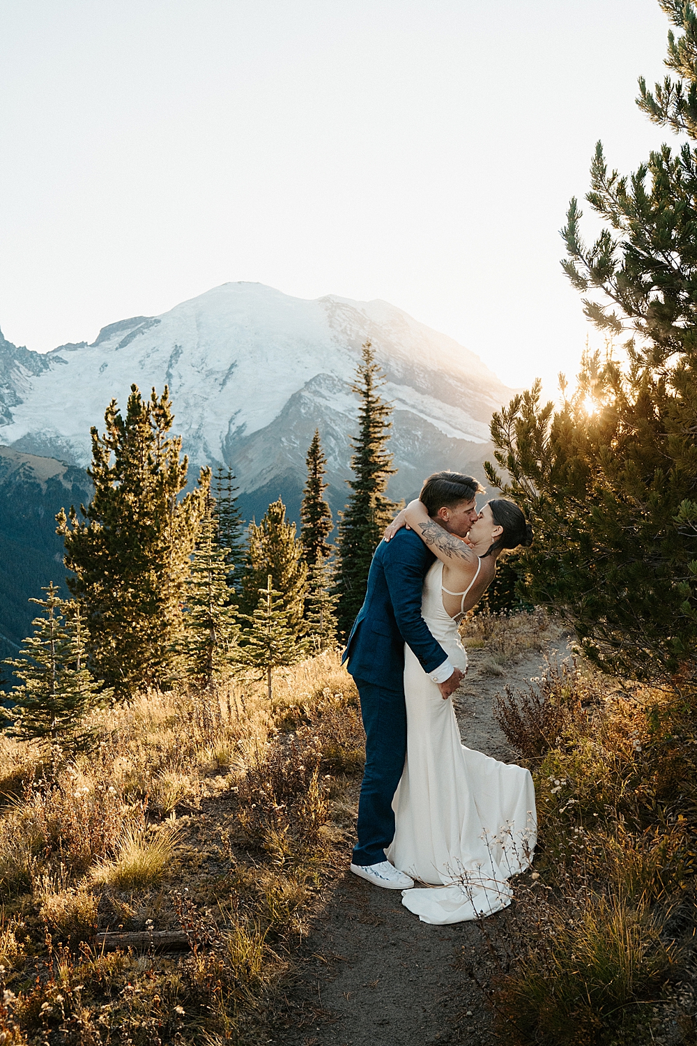 Groom kissing his bride on a trail at sunset for their Mount Rainier elopement adventure.