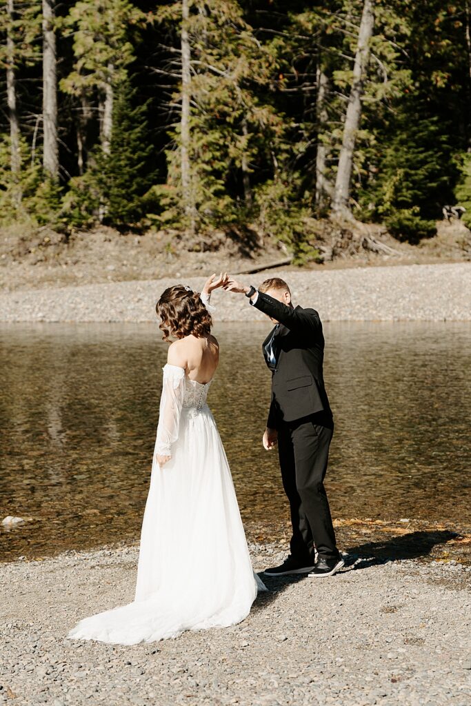 Groom in a black wedding suit twirling a bride along Avalanche Creek in Glacier Park