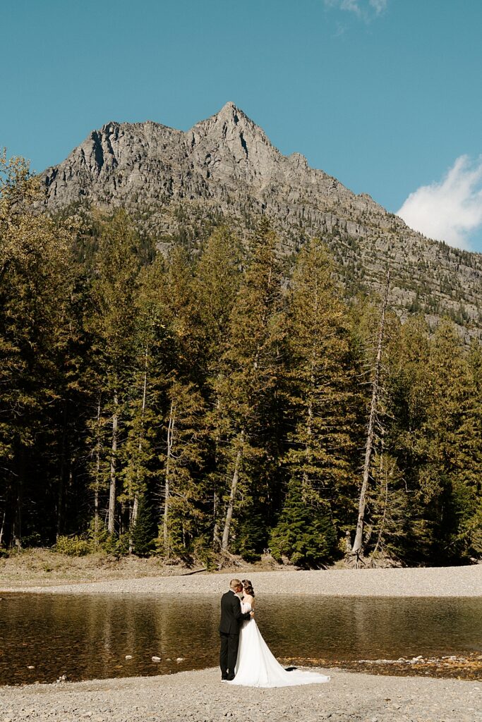 Bride and groom kissing along the river at Avalanche Creek Picnic Area for their Glacier Park small wedding celebration.