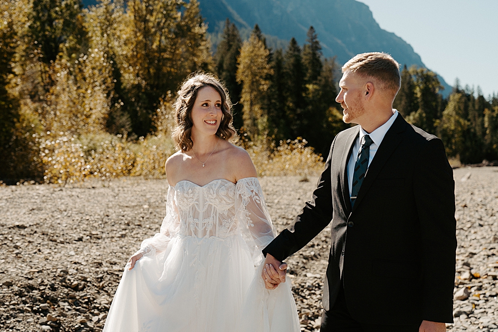 Close up of a bride and groom holding hands walking along Avalanche Creek