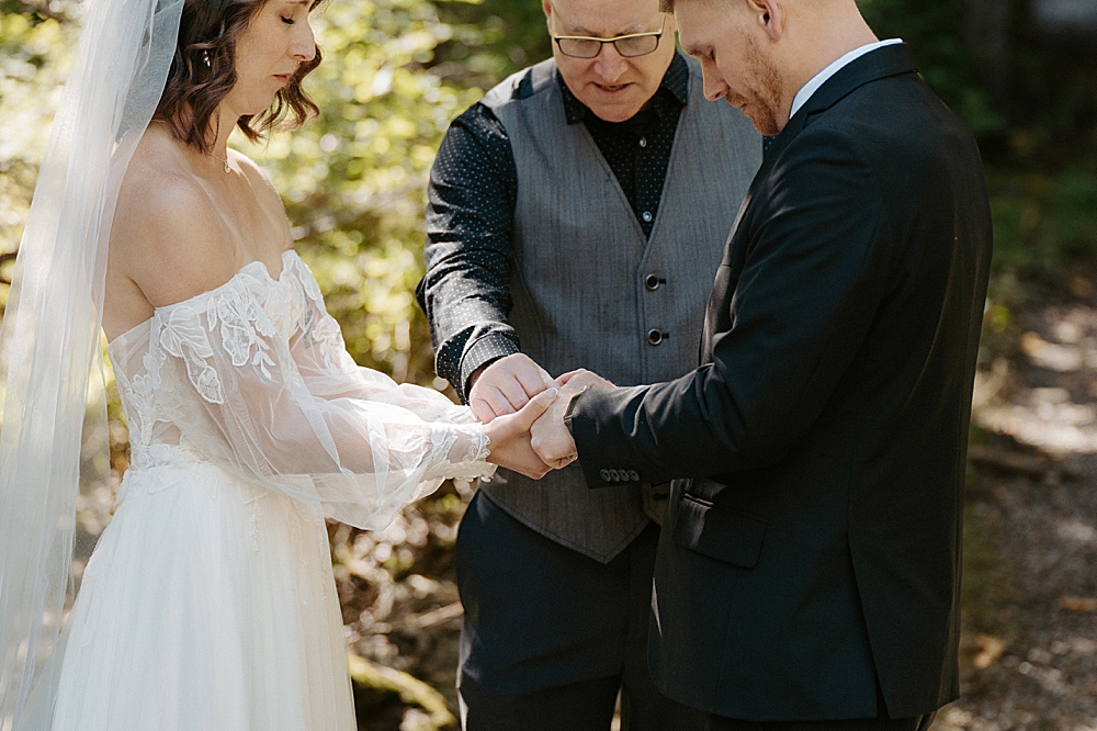 Officiant holding bride and groom's hands while praying at small wedding ceremony in Glacier Park