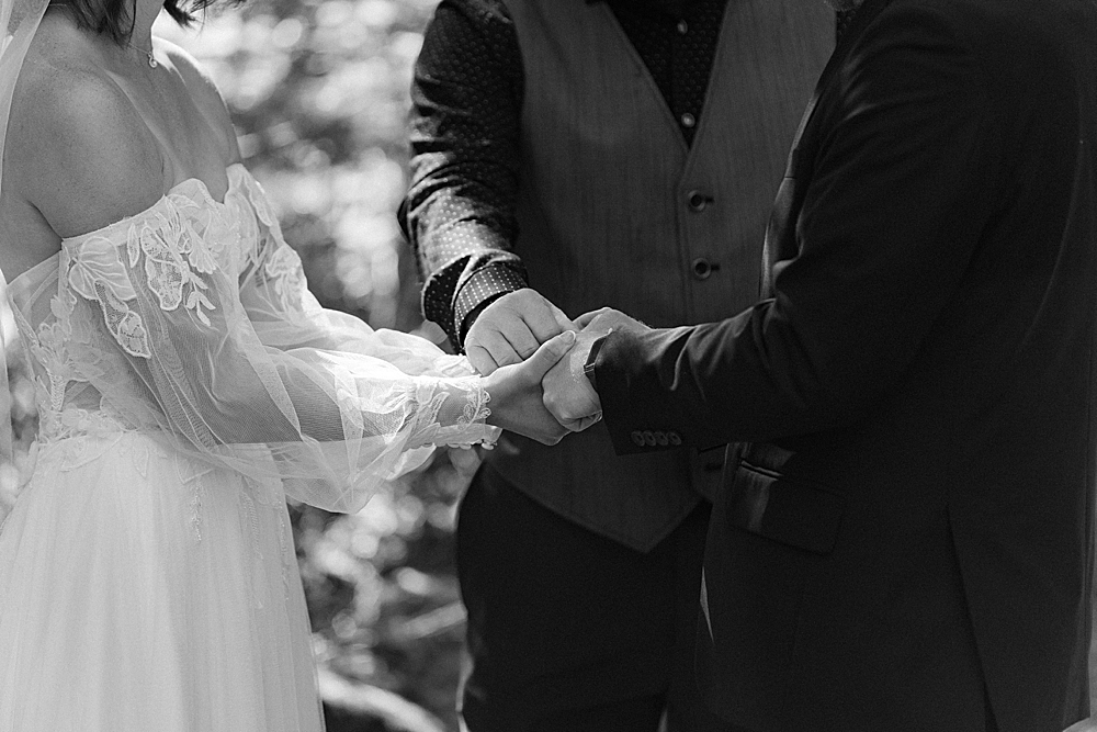 Black & white of an officiant holding bride and groom's hands while praying during an elopement ceremony