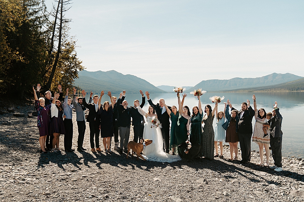 Small wedding party group photo at Lake mcDonald Lodge Beach with everyone cheering