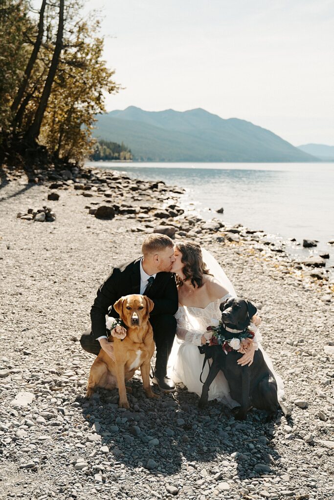 Bride and groom kissing with a brown and black lab next to them at Lake McDonald.