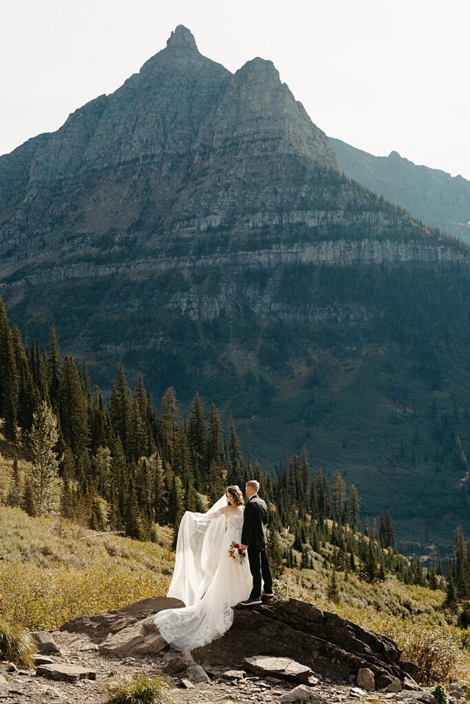 Fall elopement photo of bride and groom standing on a rock at Big Bend in Glacier