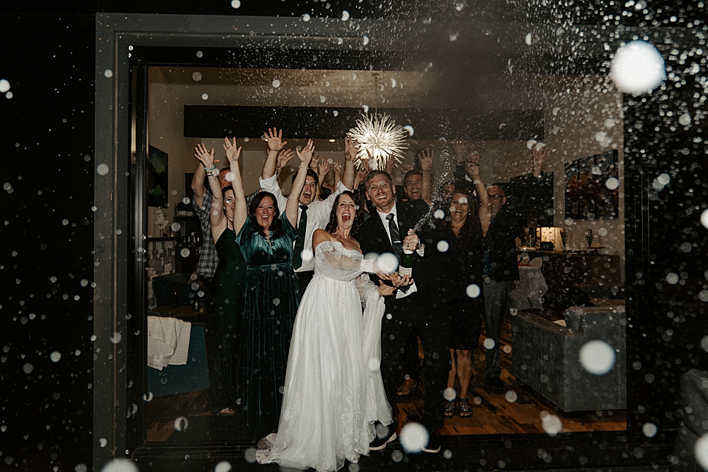 Bride and groom spraying champagne at the camera with all of their guests cheering in the background after a Whitefish wedding reception.