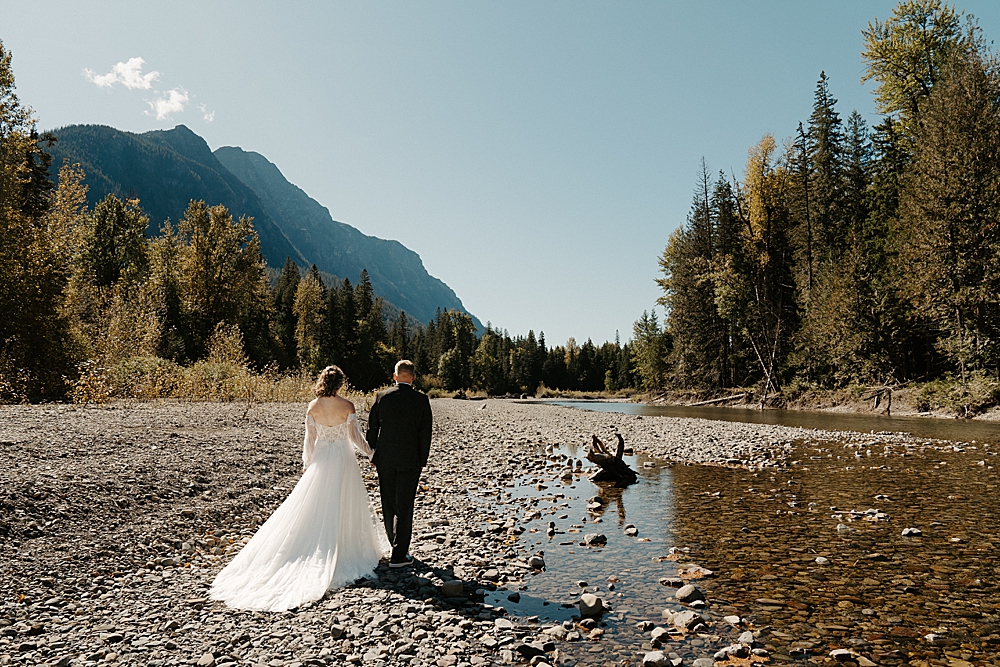 Bride and groom walking on the rocky shore at Avalanche Creek for their Glacier Park elopement