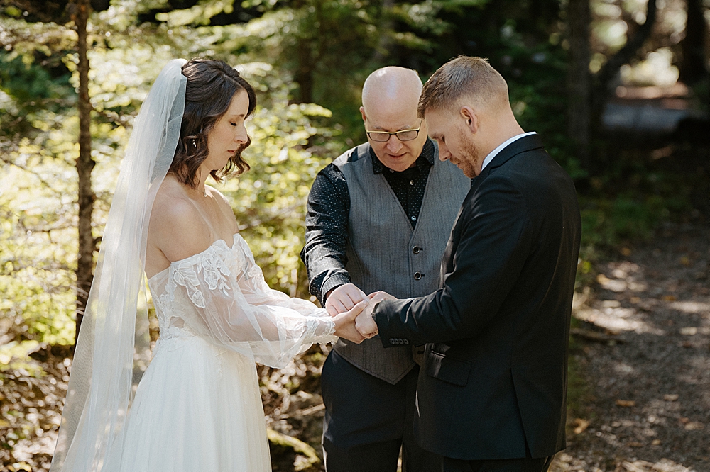 Officiant holding the bride and groom's hands and praying over them for their ceremony at Avalanche Amphitheater