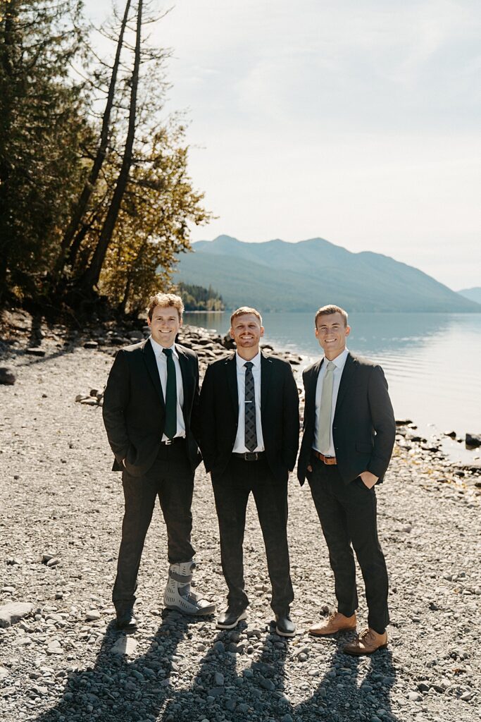 Groom and two groomsmen in black suits at Lake McDonald