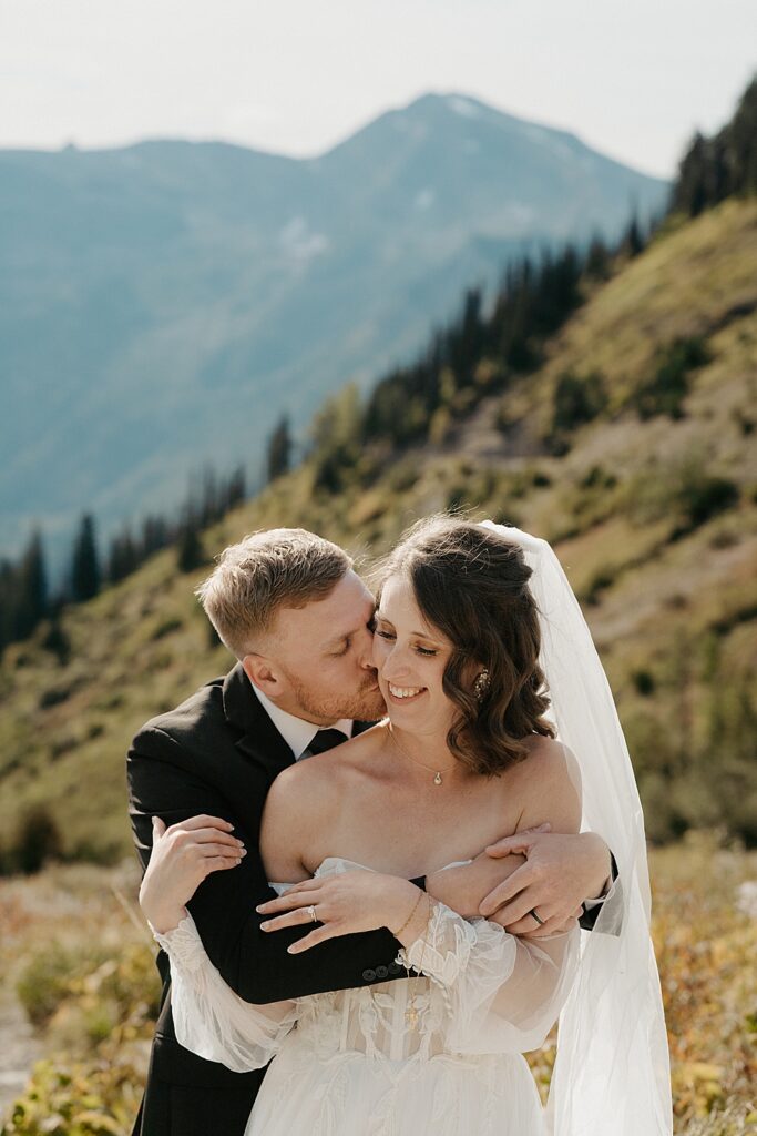 Bride and groom holding each other while groom kisses the bride's cheek at Glacier National Park
