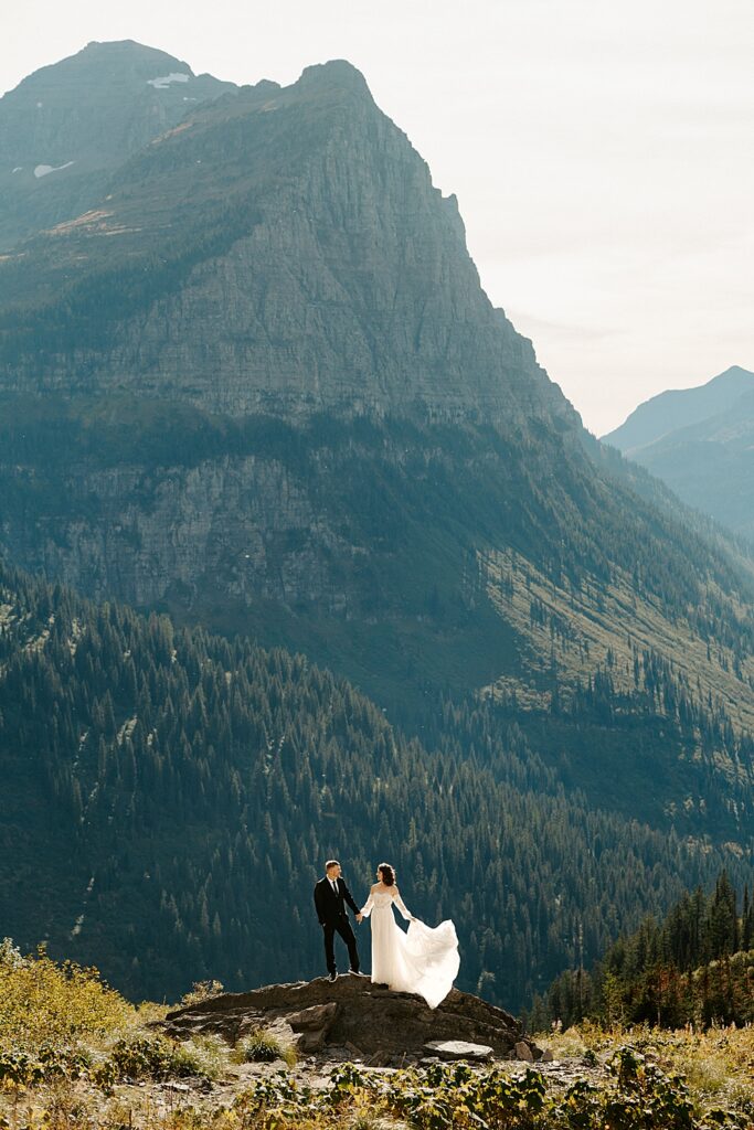 Bride and groom holding hands while standing on a rock at Big Bend in Glacier Park