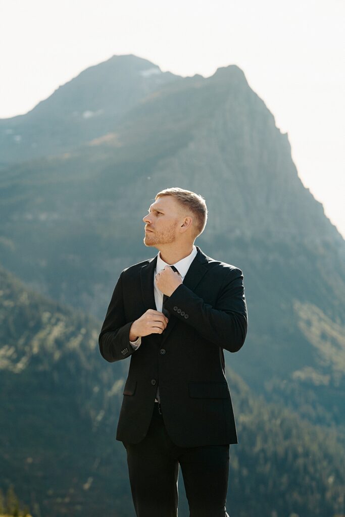 Portrait of a groom in a black suit adjusting his tie at Big Bend