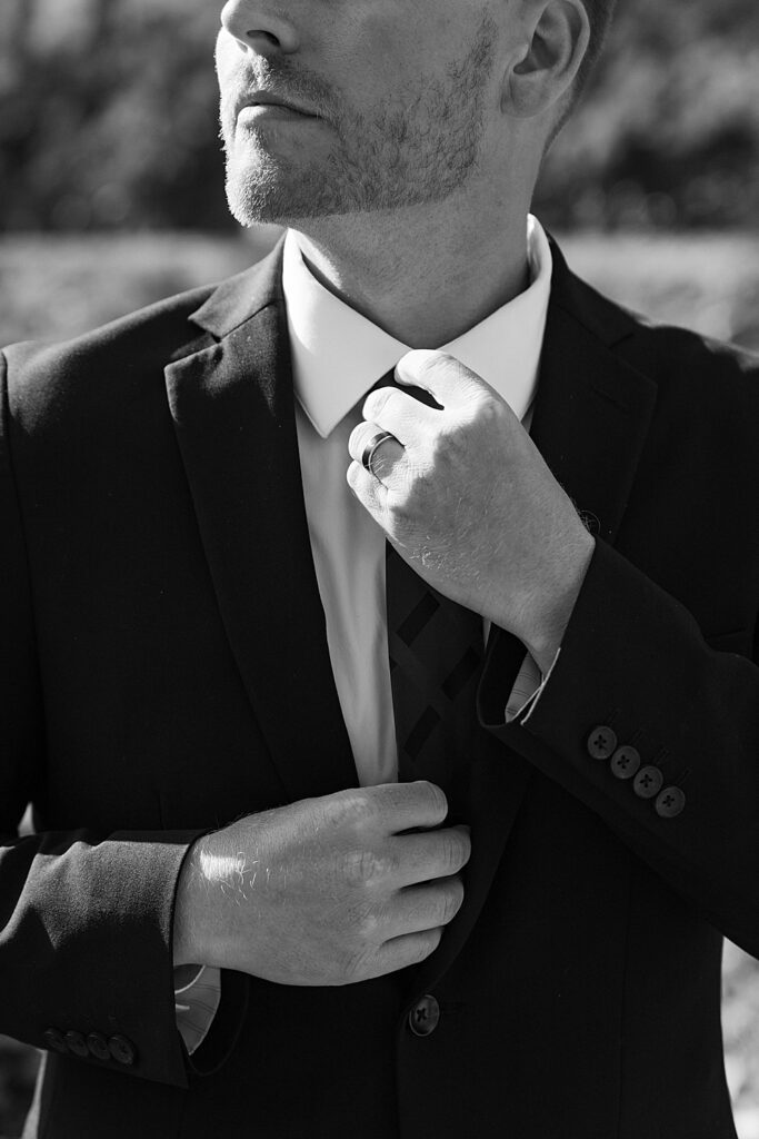 Black and white of a groom adjusting his tie