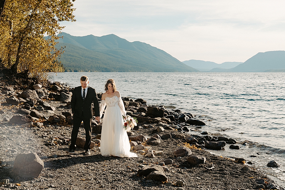 Bride and groom walking along the shore at Lake McDonald Beach at sunset