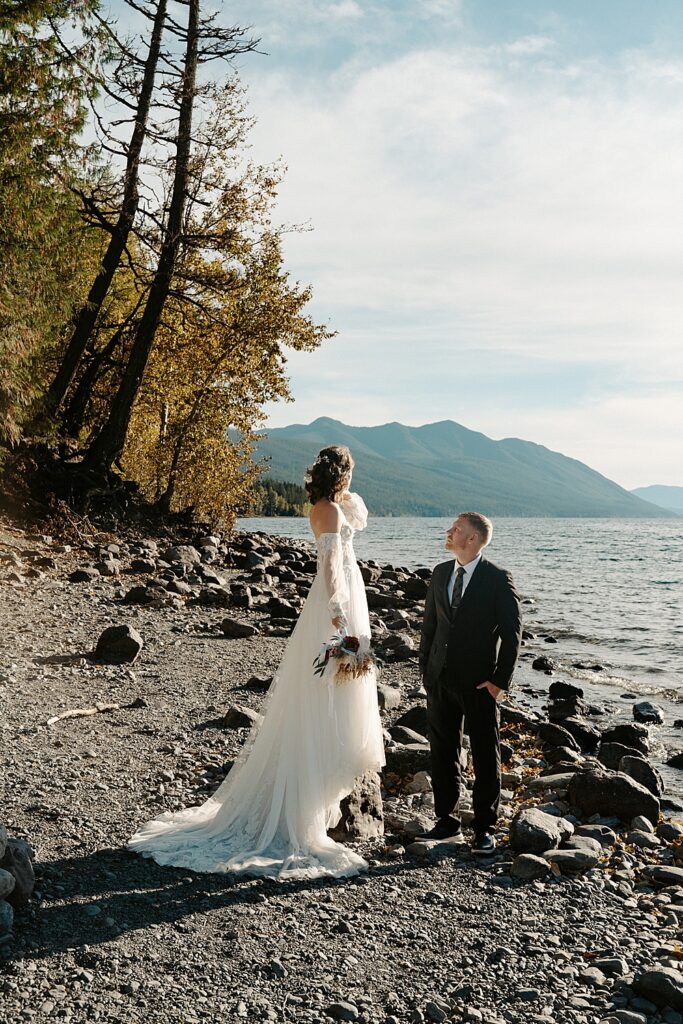 Bride and groom standing on the rocky beach of Lake McDonald at sunset