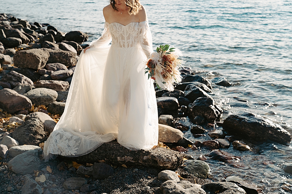 Bride walking on the rocks at Lake McDonald while holding her train and a dried floral bouquet