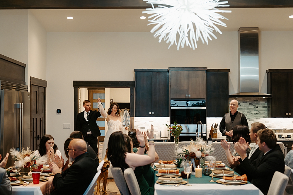 Bride and groom entering a kitchen and dining room area with guests seated at decorated tables