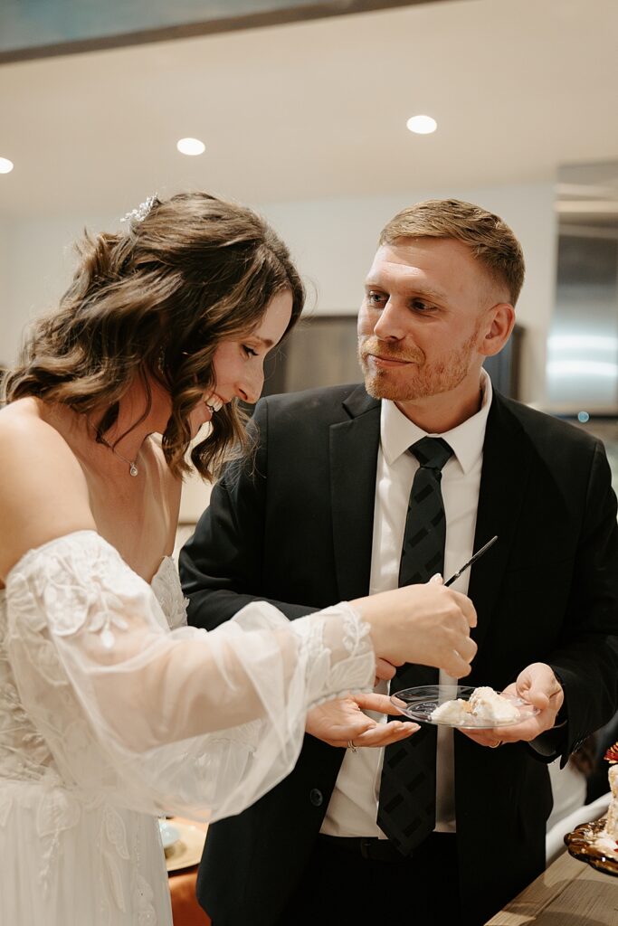 Bride and groom laughing while eating their wedding cake