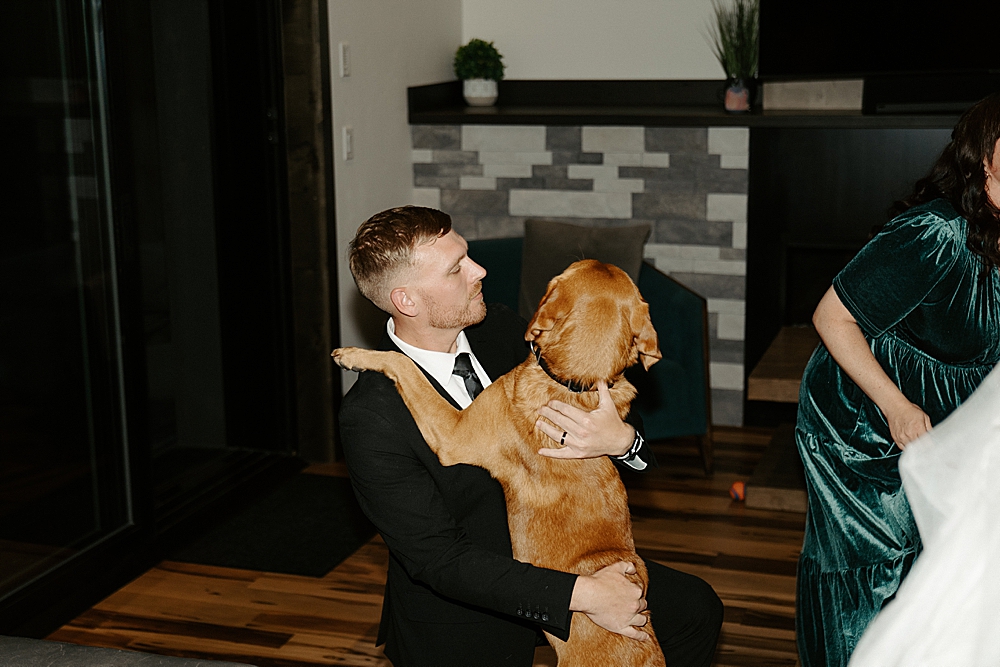 Groom kneeling down and holding onto his brown lab