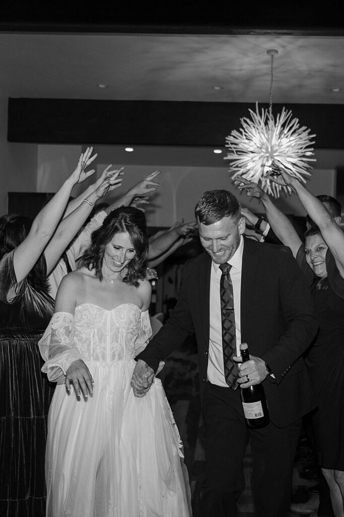Black and white of bride and groom running under a tunnel created by their wedding guests