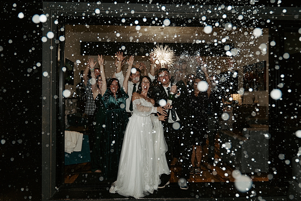 Bride and groom spraying champagne with their wedding guests cheering behind them