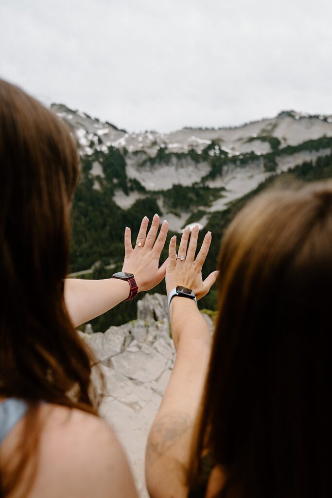 Image of two girls holding their hands in front of them to show off their engagement rings after proposing to each other in the Tatoosh Mountains.