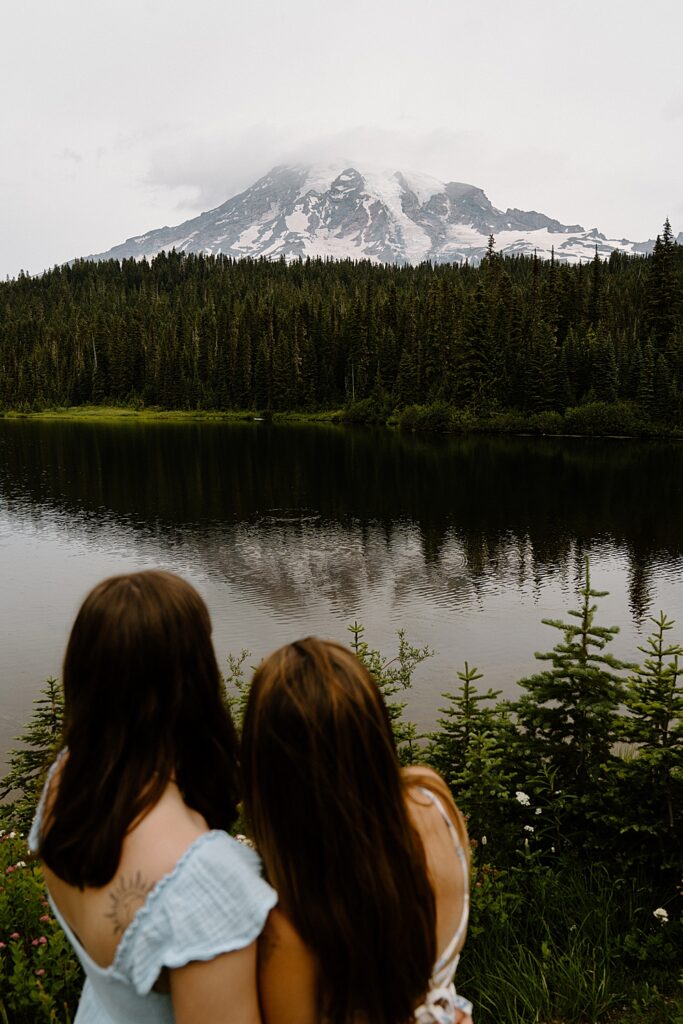 Two girls standing together in the left foreground with Mount Rainier and Reflection Lake in focus.