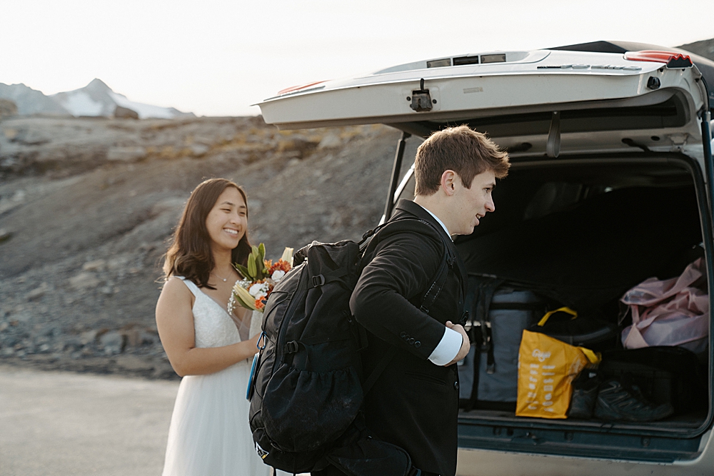 Bride helping groom get his hiking pack on for their adventure portraits at Mount Baker. 