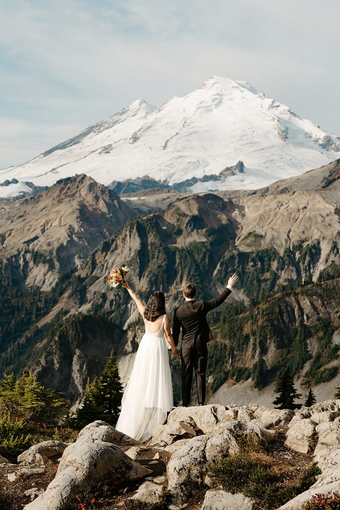 Bride and groom cheering while facing Mount Baker after their sunrise elopement.