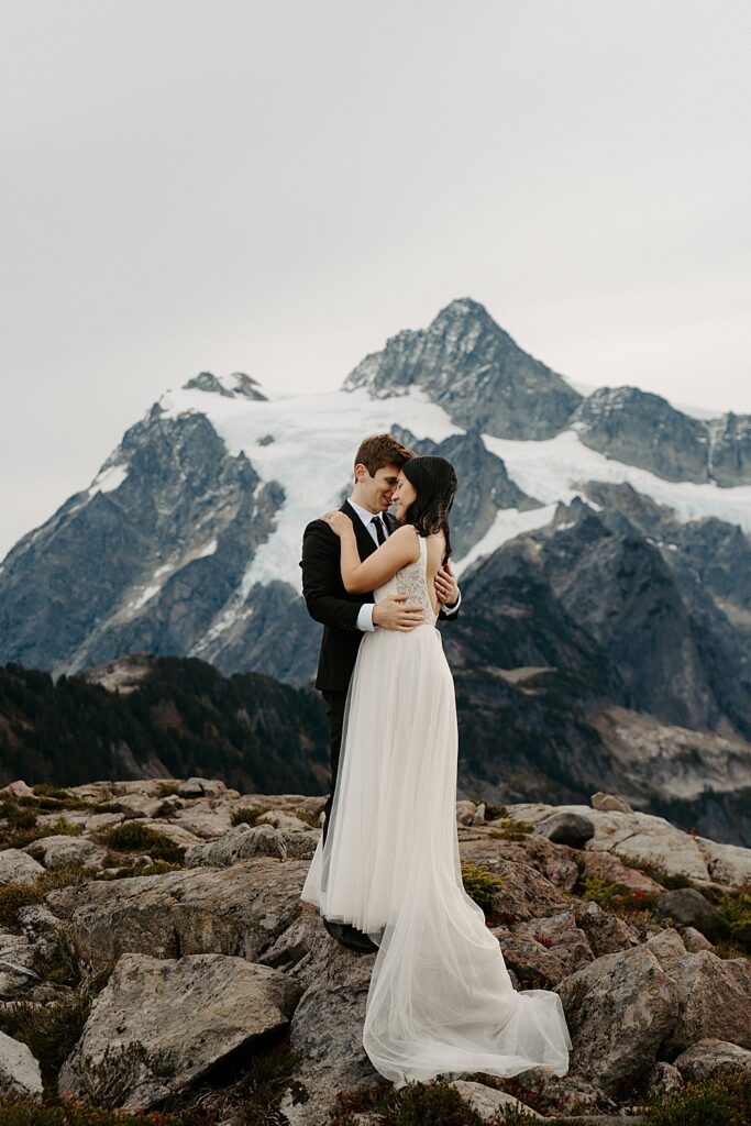 Artist Point elopement photo of a bride and groom embracing while standing on a rock with Mount Shuksan behind them. 