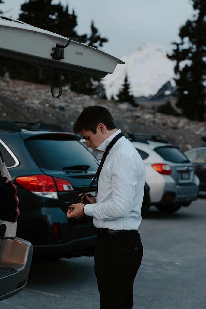 Groom getting his tie on in a parking lot before sunrise with Mount Baker in the background.